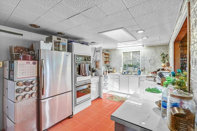 kitchen with light countertops, double oven, freestanding refrigerator, white cabinets, and light tile patterned flooring