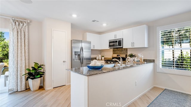 kitchen featuring stone counters, stainless steel appliances, visible vents, white cabinets, and a peninsula