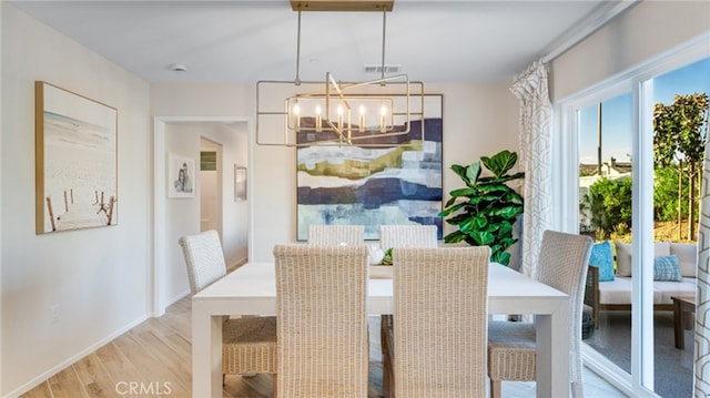 dining space featuring light wood-style floors, visible vents, a notable chandelier, and baseboards