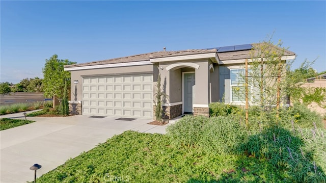 ranch-style house with driveway, stone siding, an attached garage, roof mounted solar panels, and stucco siding