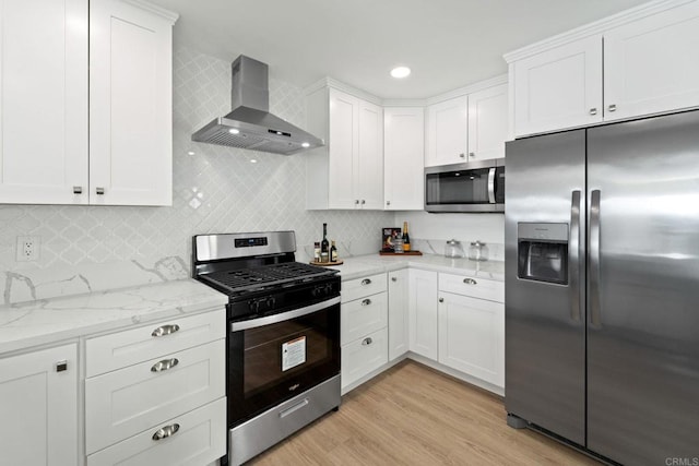 kitchen with appliances with stainless steel finishes, light wood-style floors, white cabinets, light stone countertops, and wall chimney exhaust hood