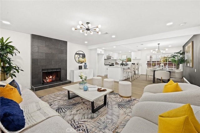 living room with a chandelier, a tile fireplace, light wood-style floors, and recessed lighting