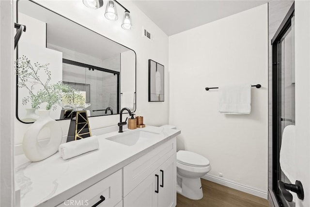 bathroom with visible vents, toilet, vanity, a shower stall, and wood finished floors