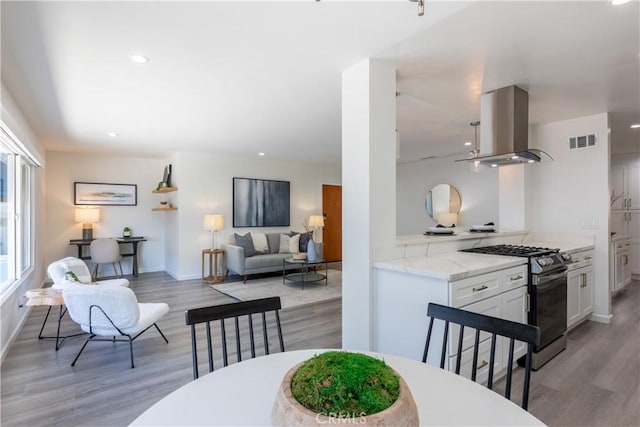 kitchen with visible vents, island range hood, white cabinets, gas range, and light wood-style floors