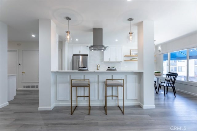 kitchen with island range hood, visible vents, white cabinets, freestanding refrigerator, and decorative backsplash