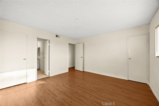 unfurnished bedroom with baseboards, a textured ceiling, visible vents, and wood finished floors