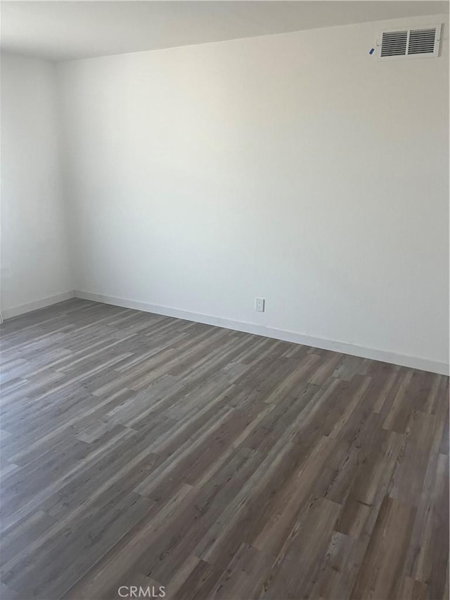 spare room featuring dark wood-style floors, visible vents, and baseboards