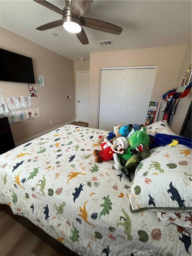 bedroom with baseboards, visible vents, a ceiling fan, wood finished floors, and a closet