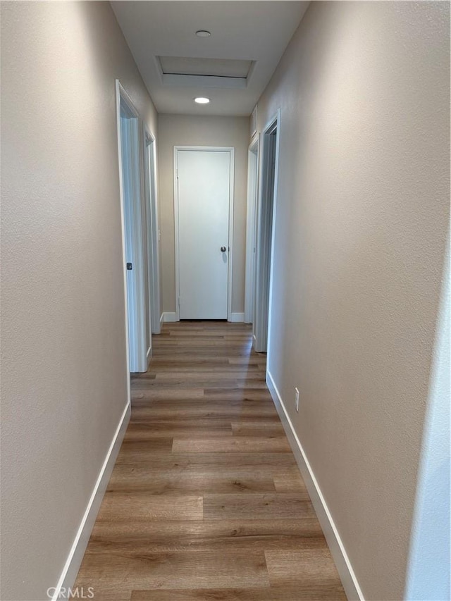 hall featuring light wood finished floors, attic access, and baseboards