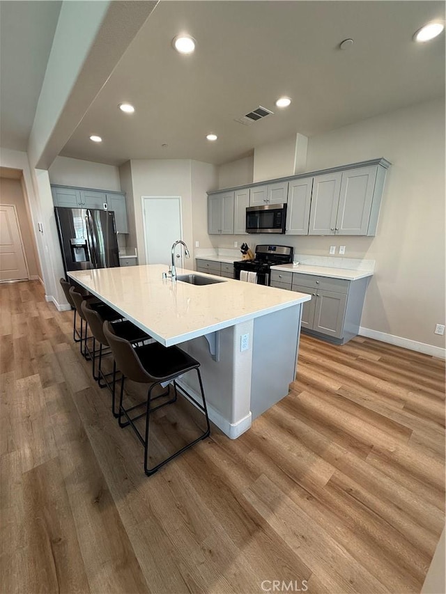 kitchen featuring light wood-type flooring, gray cabinets, stainless steel appliances, and a sink