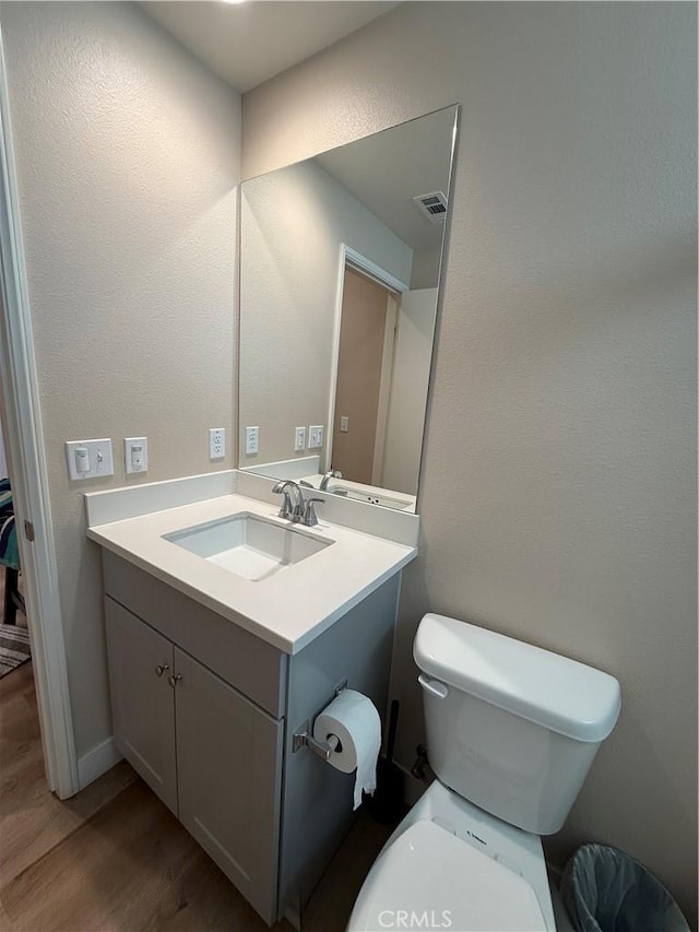 half bathroom featuring visible vents, vanity, toilet, and wood finished floors