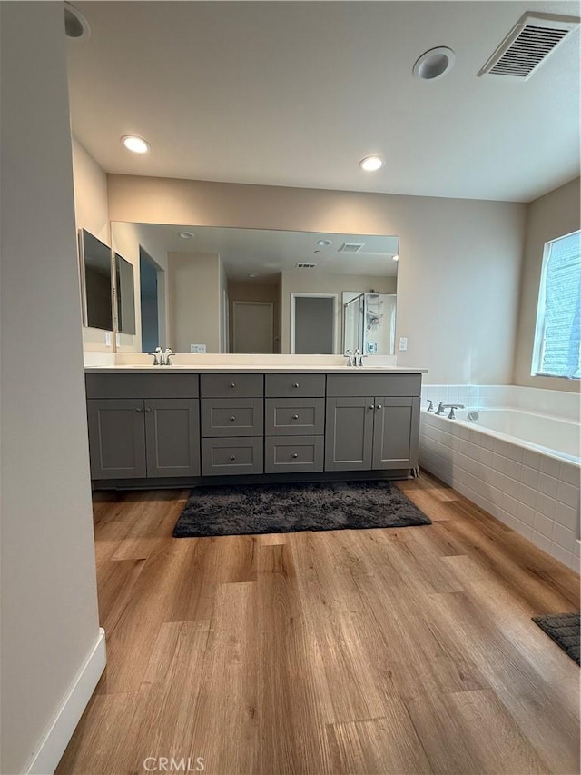 full bath with a garden tub, wood finished floors, a sink, and visible vents