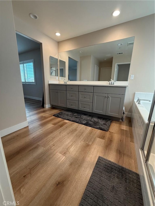 full bath with tiled tub, double vanity, baseboards, and wood finished floors