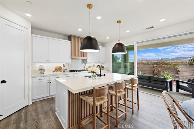 kitchen featuring black stovetop, light countertops, visible vents, dark wood-type flooring, and a sink