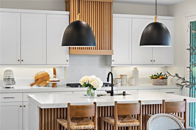 kitchen featuring a center island with sink, white cabinets, a breakfast bar, hanging light fixtures, and light countertops