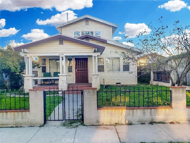 bungalow-style house with a gate, covered porch, a fenced front yard, and crawl space