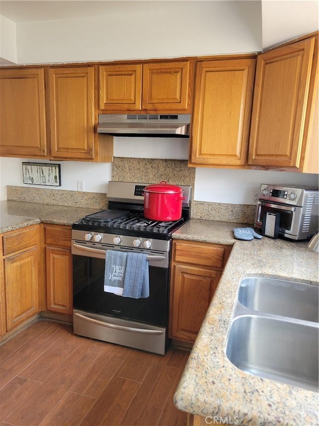 kitchen with wood finished floors, brown cabinetry, gas stove, and under cabinet range hood