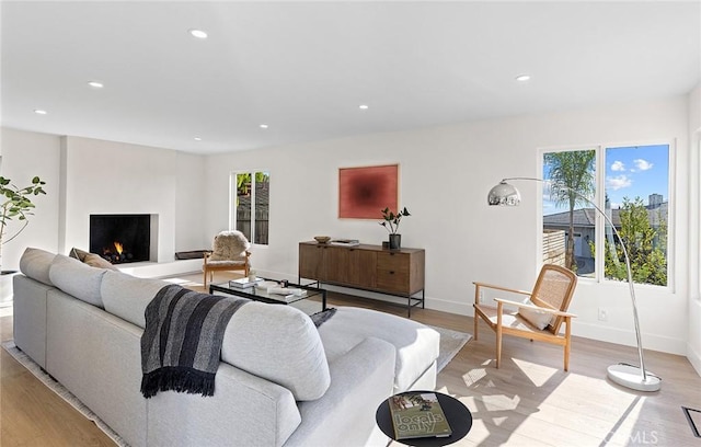 living room with a warm lit fireplace, baseboards, light wood-style flooring, and recessed lighting