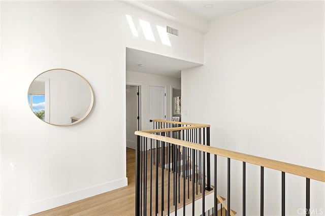 hallway with light wood-style flooring, visible vents, baseboards, and an upstairs landing