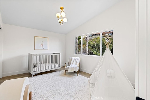 bedroom with vaulted ceiling, a crib, baseboards, and wood finished floors