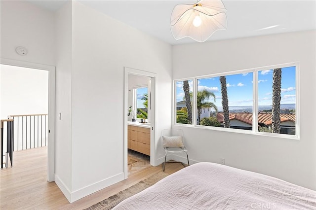 bedroom with connected bathroom, light wood-style flooring, and baseboards