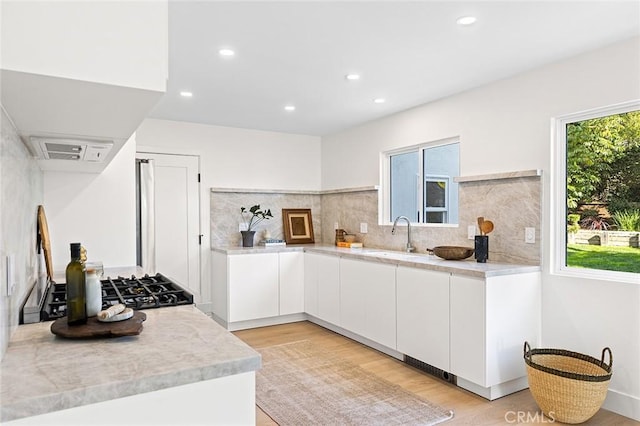 kitchen featuring light countertops, backsplash, light wood-style floors, white cabinets, and a sink