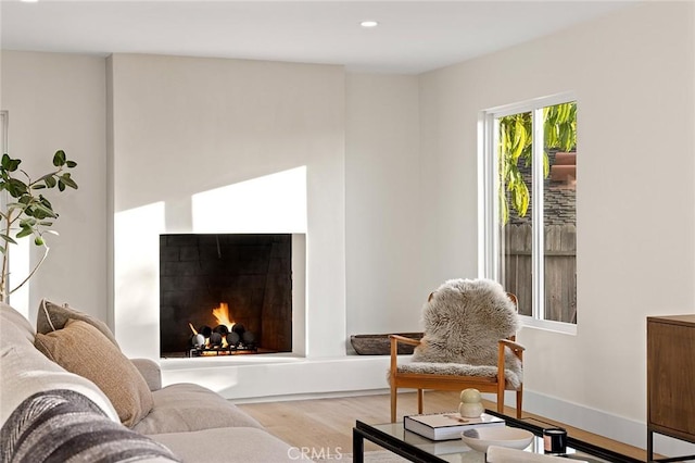 living room featuring a warm lit fireplace, baseboards, wood finished floors, and recessed lighting