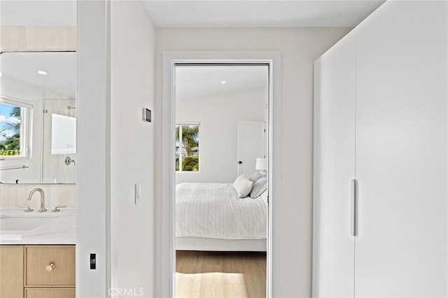 bedroom featuring wood finished floors, ensuite bath, and a sink