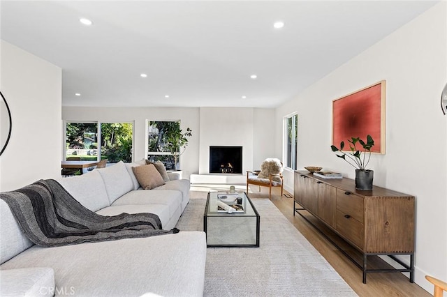 living room with light wood-style floors, a lit fireplace, baseboards, and recessed lighting