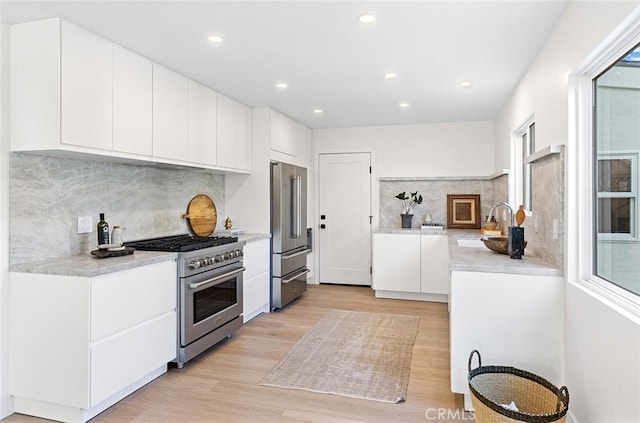 kitchen with premium appliances, light countertops, light wood-style flooring, white cabinets, and a sink