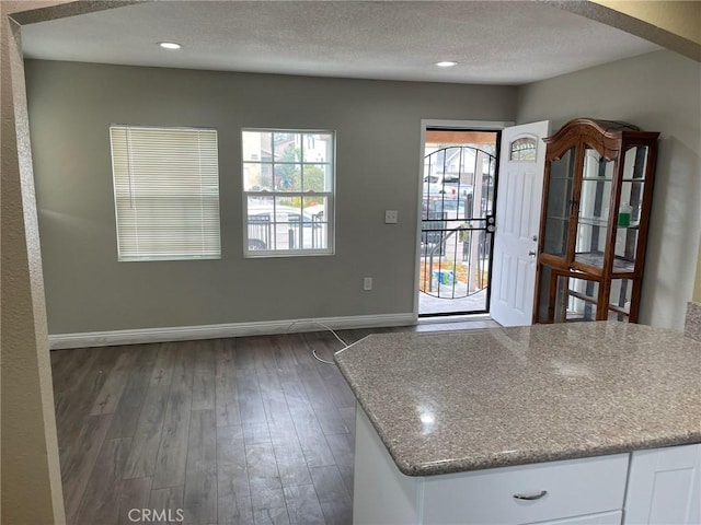 kitchen featuring baseboards, light stone counters, dark wood-style flooring, a textured ceiling, and white cabinetry