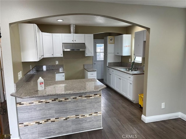 kitchen featuring dark wood-type flooring, white cabinetry, a sink, under cabinet range hood, and baseboards