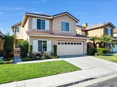 traditional home with a garage, concrete driveway, a front lawn, and stucco siding