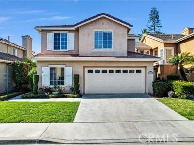 traditional home with a front lawn, driveway, an attached garage, and stucco siding