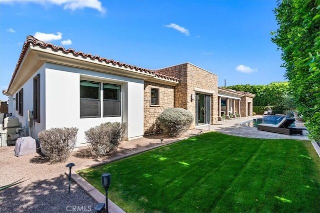 rear view of house featuring a patio, stucco siding, a lawn, stone siding, and an outdoor pool