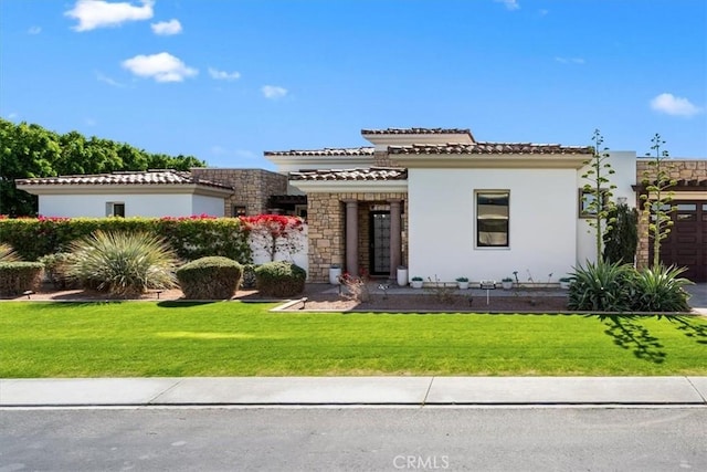 mediterranean / spanish home with stucco siding, a tile roof, stone siding, and a front yard