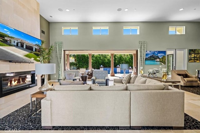 living area featuring a towering ceiling, a wealth of natural light, recessed lighting, and a tile fireplace