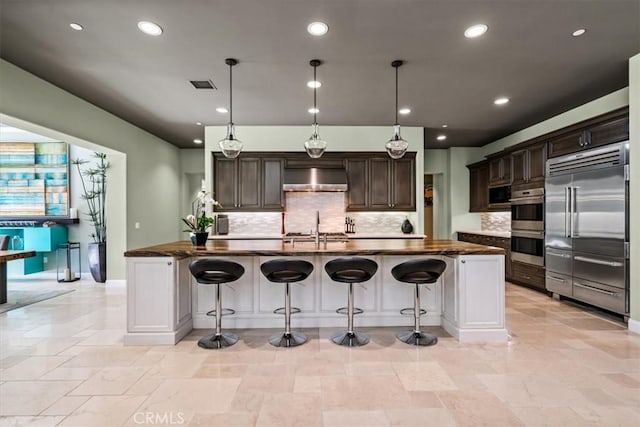 kitchen with wall chimney range hood, decorative backsplash, dark countertops, stainless steel appliances, and dark brown cabinetry