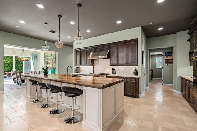 kitchen featuring dark brown cabinetry, decorative backsplash, under cabinet range hood, stainless steel gas cooktop, and recessed lighting