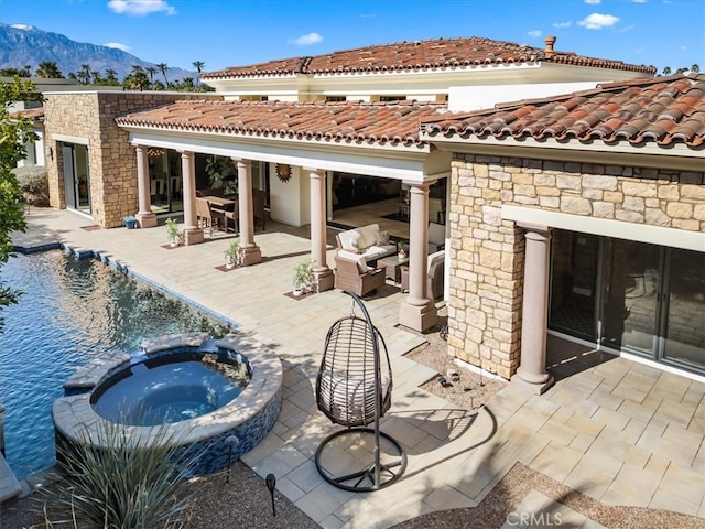 back of house featuring stone siding, a tiled roof, a patio area, a pool with connected hot tub, and a mountain view