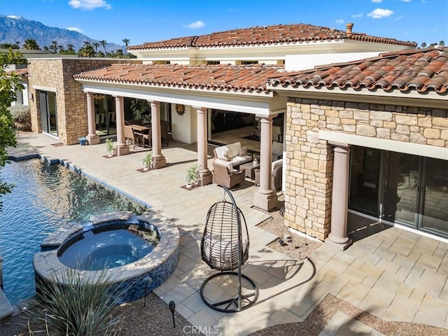back of property featuring a tile roof, a pool with connected hot tub, a patio area, a mountain view, and stone siding