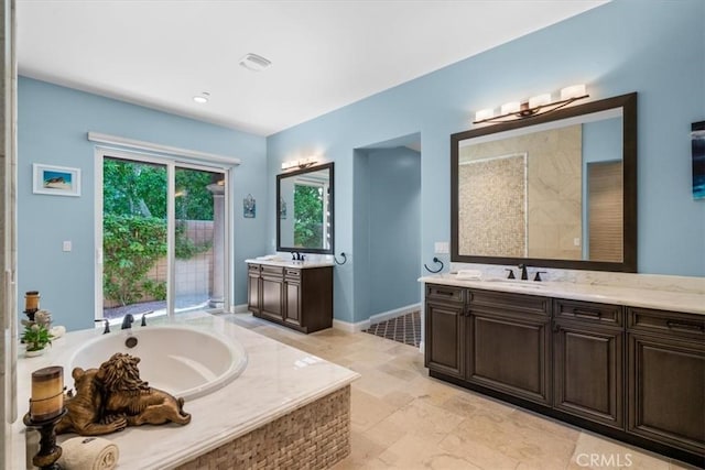 bathroom with a wealth of natural light, a garden tub, two vanities, and a sink