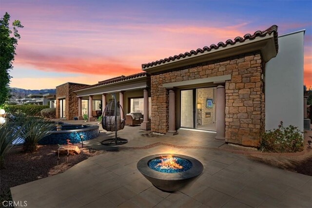 rear view of house featuring a patio, an outdoor fire pit, a tile roof, stone siding, and stucco siding