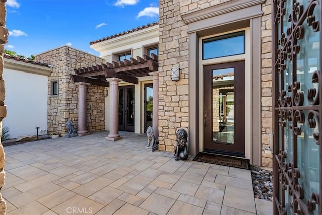 view of exterior entry with stone siding, a pergola, and a patio