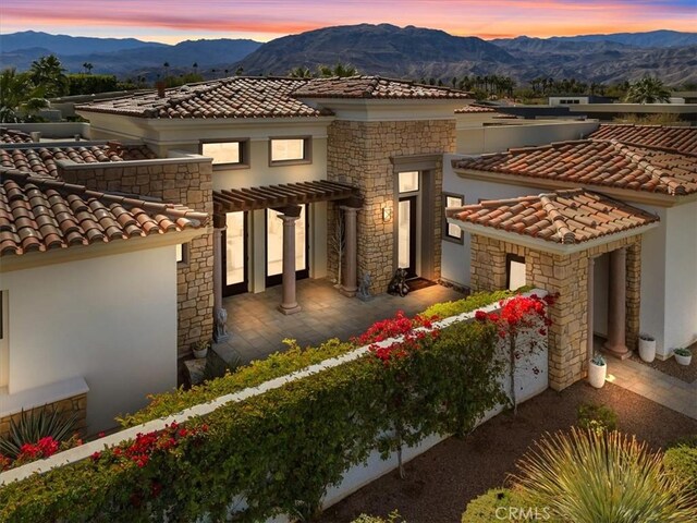 view of front of property featuring stone siding, a tiled roof, a mountain view, a pergola, and stucco siding