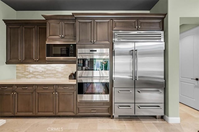 kitchen with built in appliances, dark brown cabinets, light countertops, and decorative backsplash