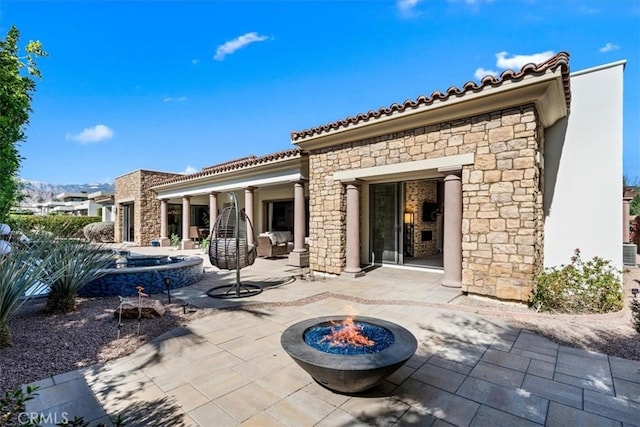 rear view of property featuring an outdoor fire pit, stone siding, a tile roof, a patio area, and stucco siding