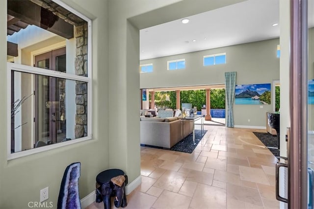 interior space featuring a towering ceiling, baseboards, stone tile flooring, and recessed lighting