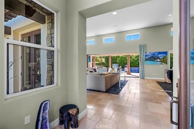 hallway featuring baseboards, recessed lighting, stone tile flooring, and a high ceiling