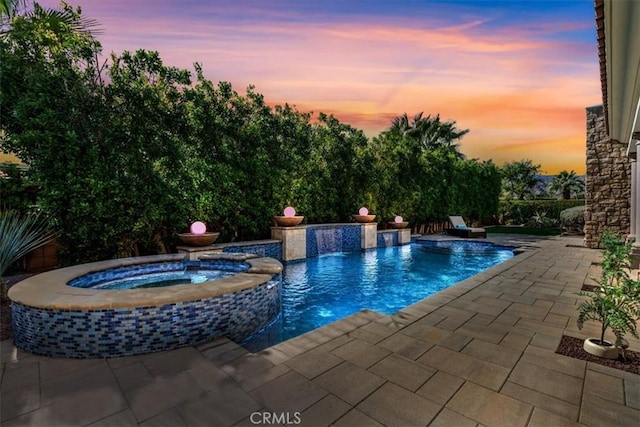 pool at dusk with a patio area and a pool with connected hot tub